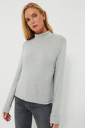 A woman wears a DONNI. light heather grey sweater turtleneck with a relaxed fit and dark gray jeans, highlighting the soft sweater fabric.