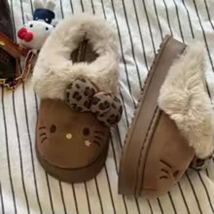 Pair of brown slippers with cat face design on a striped fabric background