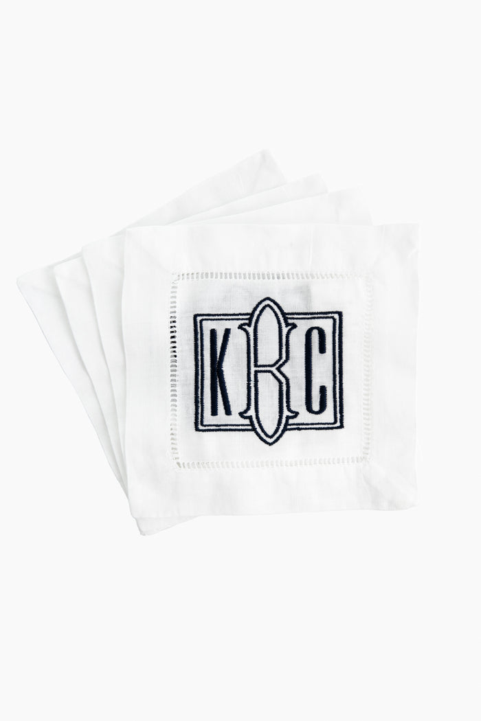 A stack of Caton's Wharf white Hemstitched Cocktail Napkins, each with an embroidered "K C" monogram and black eyeglass outline—an ideal personalized gift.