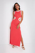A woman poses gracefully in a retro-inspired look, wearing the STAUD sleeveless, floor-length coral maxi dress featuring white circular accents at the waist.