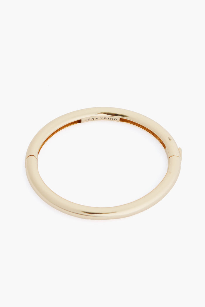 The Jenny Bird Gia Bangle is a simple, round 14K gold tone bracelet featuring a subtle engraved logo inside—perfect for adding elegance to your jewelry collection.