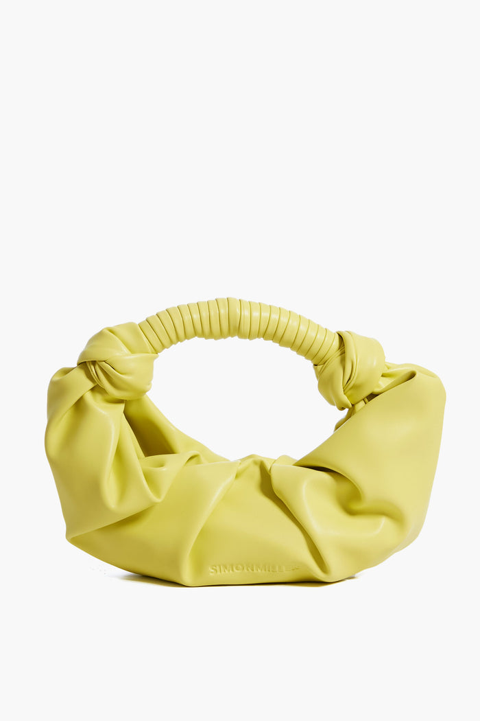 Simon Miller's yellow ruched shoulder bag features a textured, wrapped handle and is crafted from vegan leather, making it a striking statement purse.