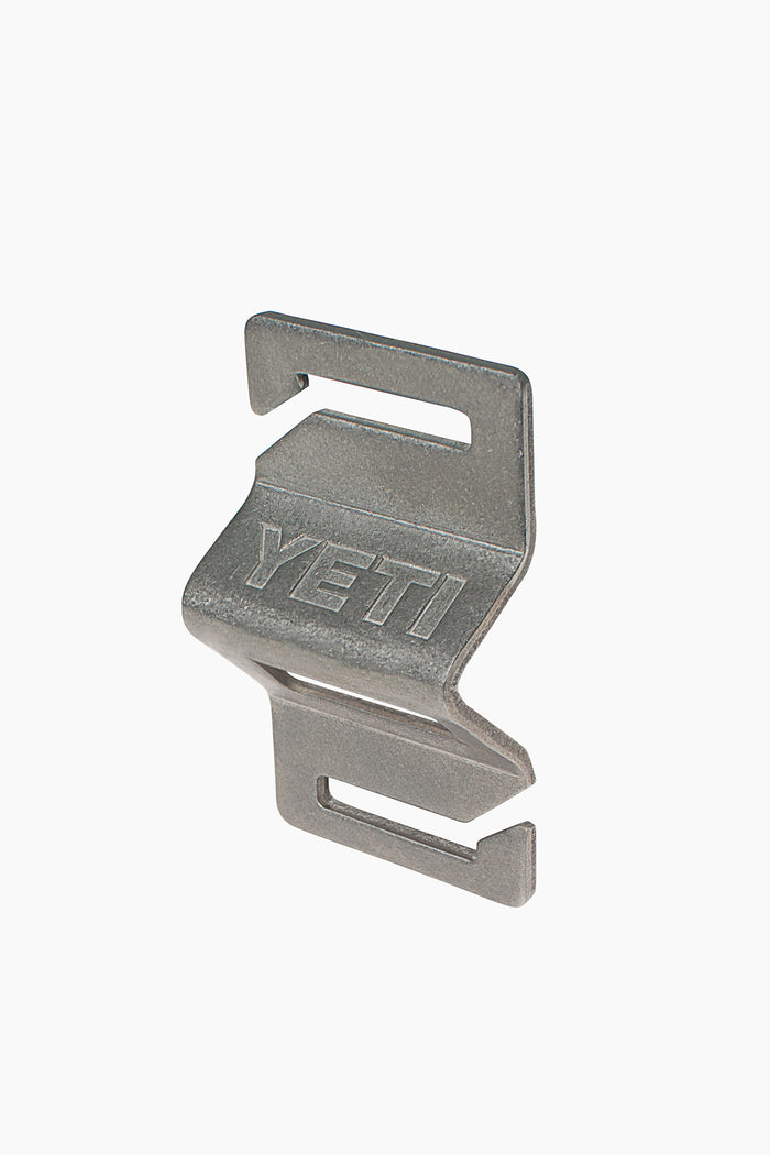 The YETI gray stainless steel clip features two slots, an angled design, and embossed YETI branding—compatible with a MOLLE bottle opener and perfect for your YETI cooler.