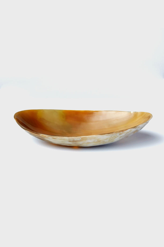 The Be Home oval-shaped, shallow horn bowl features a polished amber-toned surface and smooth texture. Handcrafted and ethically sourced, it's perfect for those who appreciate unique home goods.