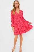 Woman wearing a Hot Pink Ikat Pomander Place dress featuring long sleeves, zigzag pattern, V-neckline, tiered skirt, and flutter smocked cuffs.