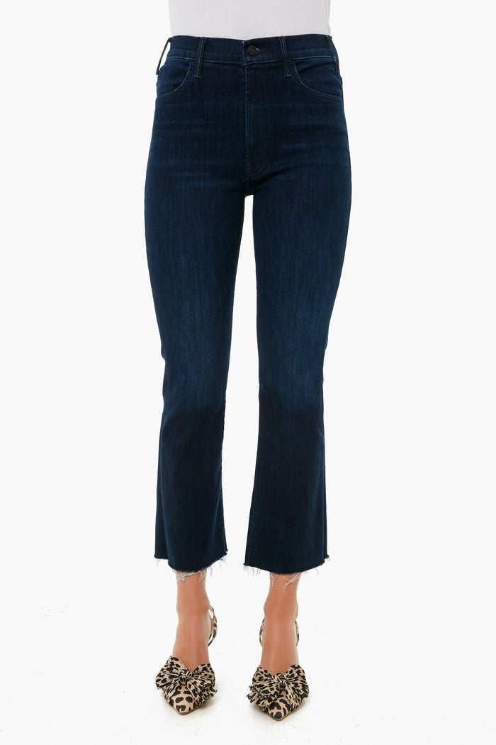A person wears MOTHER dark blue cropped ankle jeans with a raw hem, paired with leopard print heels, highlighting the brand’s stylish denim fit.