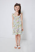 A young girl in an Angel Dear smocked ruffle dress and white sandals stands confidently, with pink sunglasses resting on her head.