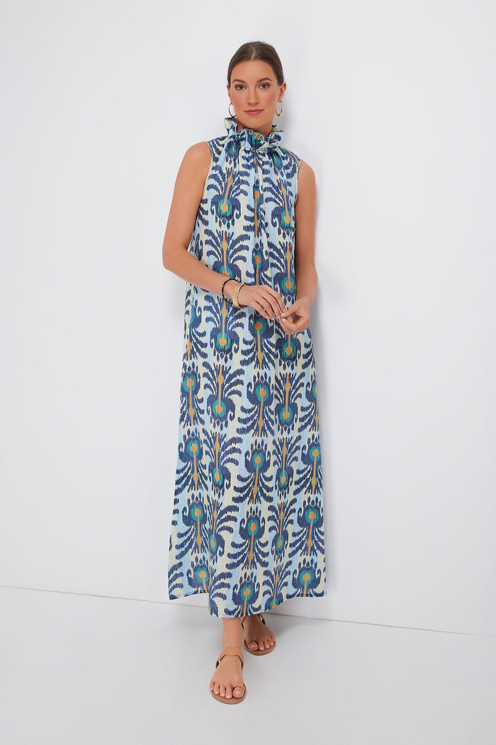 A woman wears the Nimo With Love Ikat Blue Sundrop Dress, a sleeveless linen maxi dress in blue, green, and orange abstract print, paired with tan sandals.