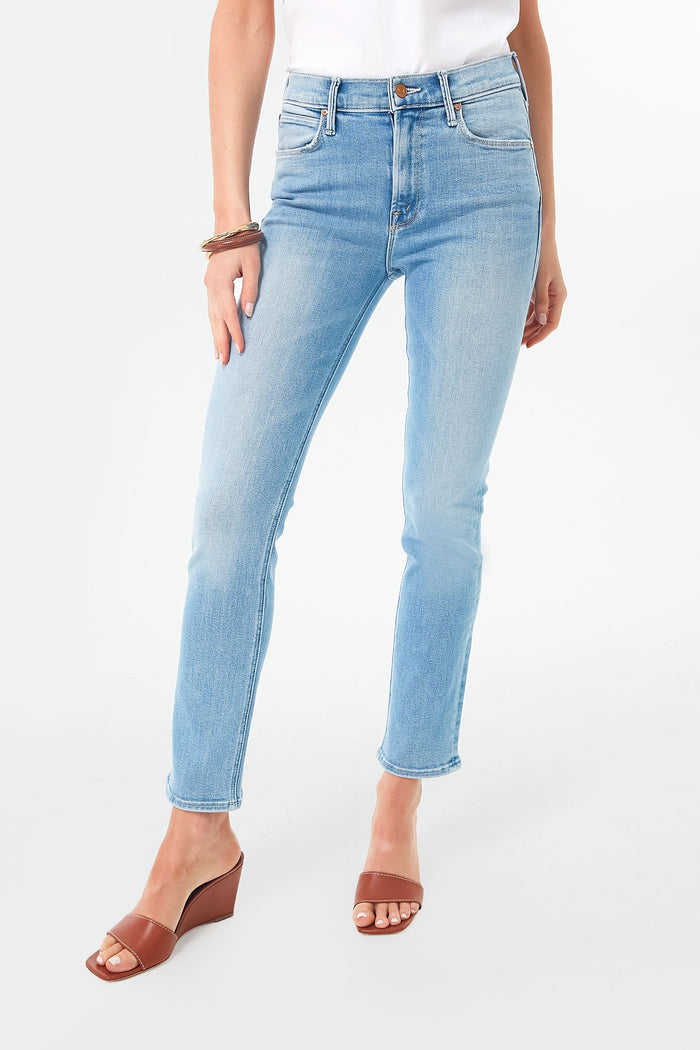 A person stands confidently, wearing light blue MOTHER straight leg jeans, a white top, brown heeled sandals, and bracelets.