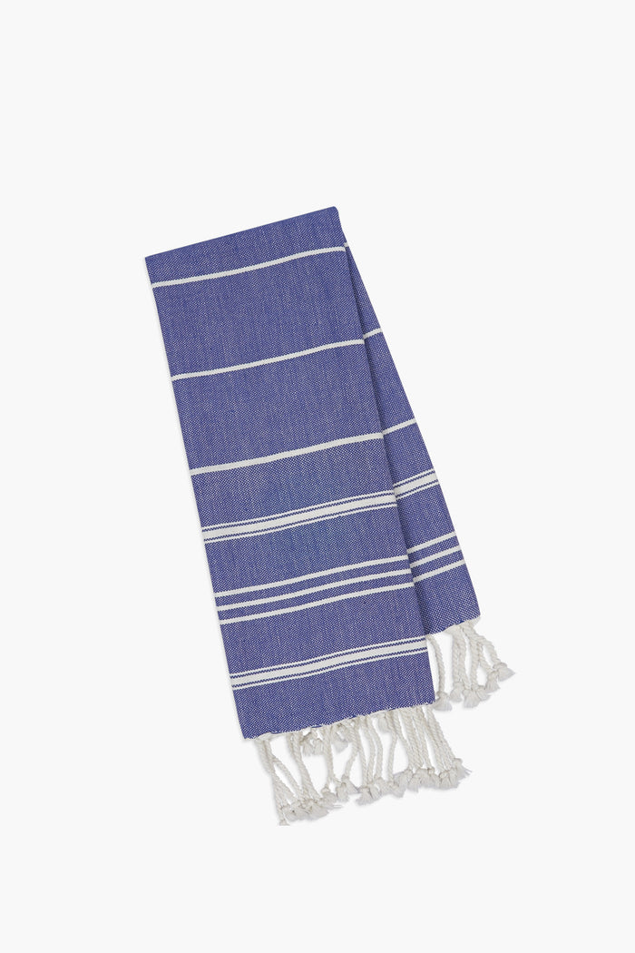A folded blue and white striped Caton's Wharf Indigo Fouta Kitchen Towel with fringed edges—perfect as a stylish Turkish kitchen towel or thoughtful monogrammed home gift.