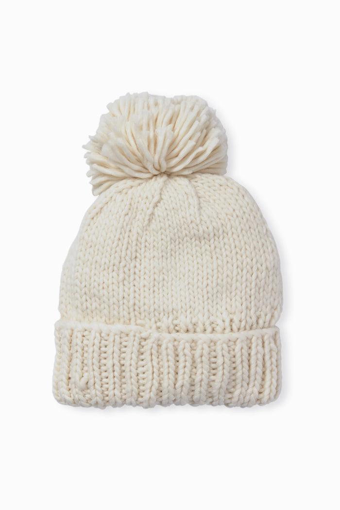 The Look by M hand-knit beanie features a soft cream color, a large pom-pom on top, and a cozy textured design.