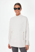 A woman in Varley activewear—a light mock neck zip sweatshirt and dark leggings—smiles at the camera, wearing dark sunglasses.