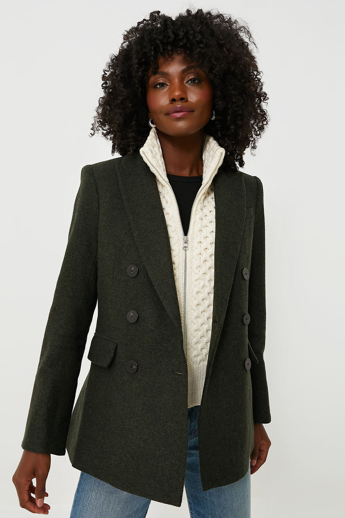 A woman wears a Veronica Beard dark green wool double-breasted blazer over a cream cable knit dickey and blue jeans.