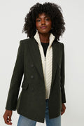 A woman wears a Veronica Beard dark green wool double-breasted blazer over a cream cable knit dickey and blue jeans.