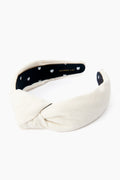 The Lele Sadoughi ivory cotton headband features a front knot and a black inner lining with small white flower patterns.