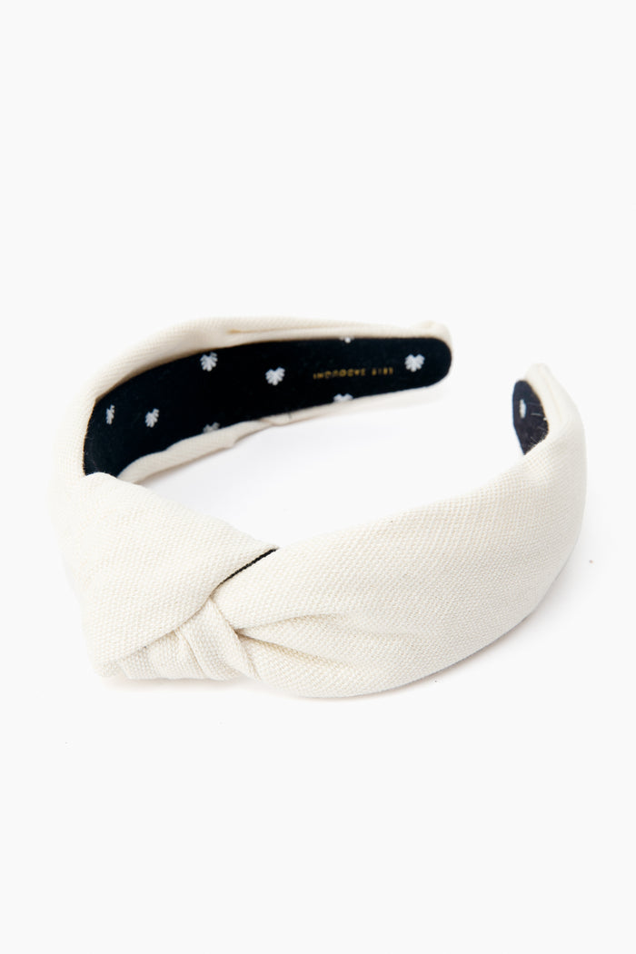 The Lele Sadoughi ivory cotton headband features a front knot and a black inner lining with small white flower patterns.