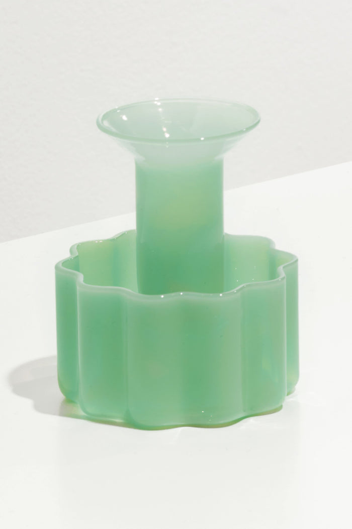 The FAZEEK Jade Wave Candle Holder features a translucent light green hue, wide flared opening, and scalloped geometric base. Both functional and decorative, this sculptural piece sits elegantly on any surface.