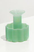 The FAZEEK Jade Wave Candle Holder features a translucent light green hue, wide flared opening, and scalloped geometric base. Both functional and decorative, this sculptural piece sits elegantly on any surface.