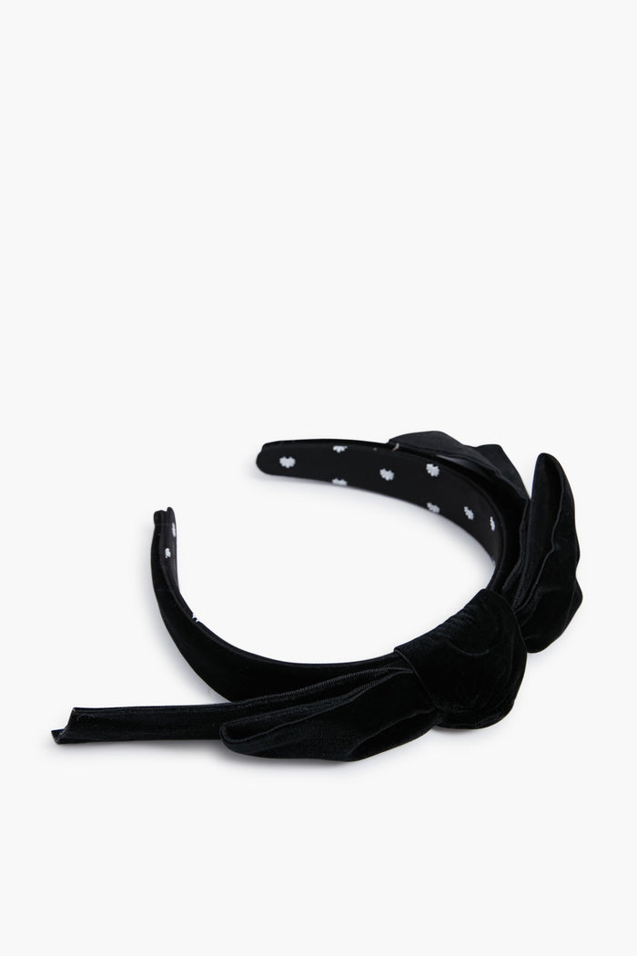 A black Lele Sadoughi velvet headband with a large bow and an inner lining printed with small white flowers.