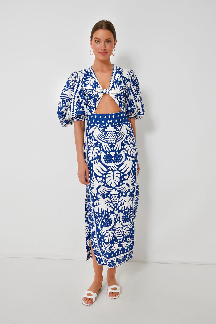 A woman models Farm Rio’s Jungle Scarf Navy Dress—a blue and white patterned style with puffed short sleeves, front cutout, and white sandals—highlighting sustainable fashion.