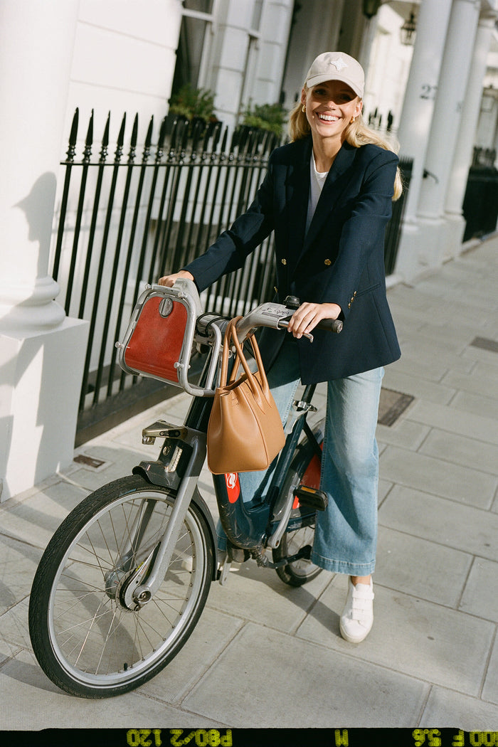 A young woman effortlessly sports the classic Khaki Collegiate Hat, adding a fun, high-end touch to her casual city bike outing ensemble.