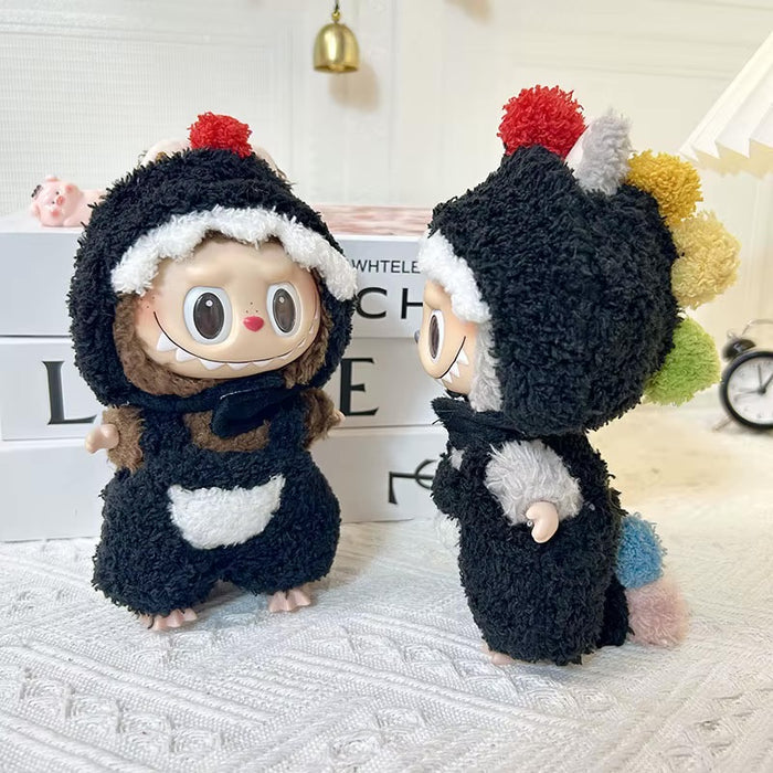 Two plush toy figures dressed in fuzzy black outfits with white trim and colorful pom-pom accents, posed on a white textured surface in a styled indoor setting.