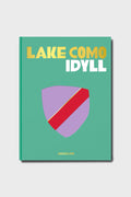 Assouline’s “Lake Como Idyll” book cover features gold and white text with a minimalist purple and red shield design—ideal for those inspired by Lake Como and Italian luxury vacations. The Assouline brand is noted at the bottom.