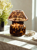 Decorative glass lamp style candle with a leopard print pattern on a marble surface.
