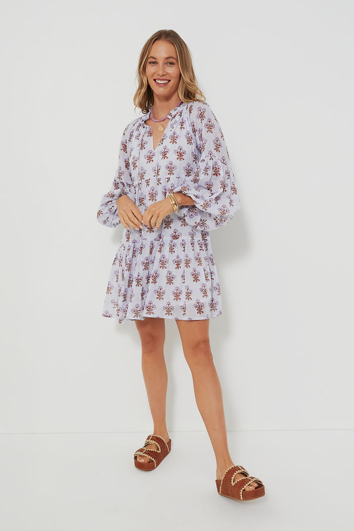 Woman in an Oliphant light-colored, long-sleeve boho mini dress with floral prints, paired with brown sandals with gold buckles.