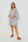 Woman in an Oliphant light-colored, long-sleeve boho mini dress with floral prints, paired with brown sandals with gold buckles.
