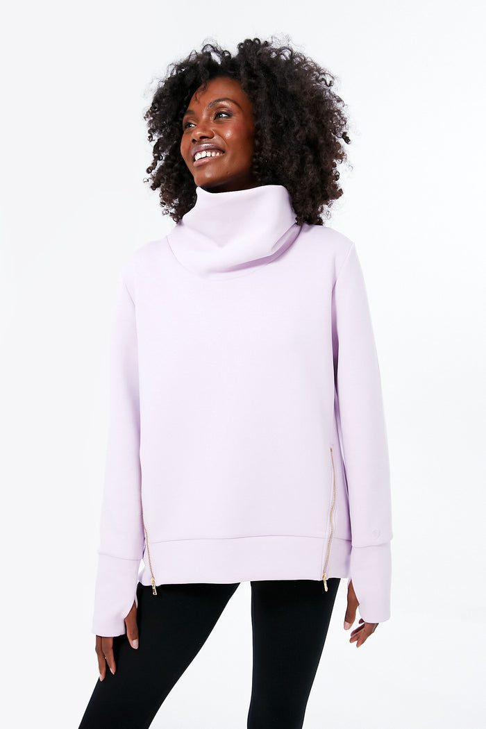 A woman wears the Addison Bay light purple funnel neck sweatshirt with side zippers and black leggings, ideal as an everyday pullover and for athleisure wear.