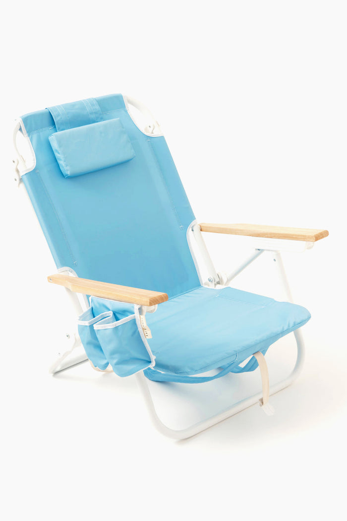 The Sunnylife light blue folding beach chair features wooden armrests, a small pillow, adjustable recline, and an insulated cooler pocket.