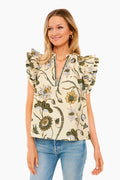 A woman in a Ulla Johnson short-sleeve floral cotton poplin blouse with ruffled shoulders and light blue jeans smiles brightly.