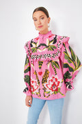 A woman wears a Farm Rio Leopard Forest Pink Blouse with bold floral and animal prints and ruffled details, paired with light blue jeans, adding vibrant flair to her look.