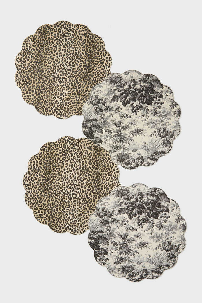 Four scalloped round reversible placemats by Tuckernuck Home: two with leopard print and two with black and white tropical foliage. Made from wipeable polyurethane leather for easy care.