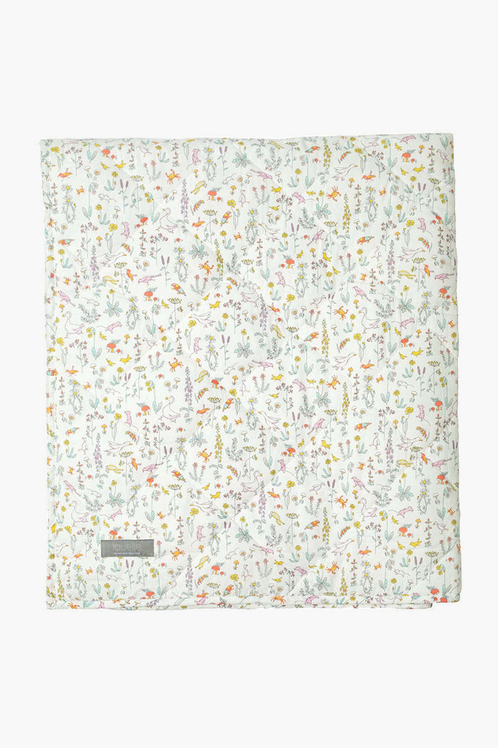 A folded Louelle. white quilt with a colorful floral pattern, small flowers and leaves, plus a gray corner label makes a charming linen play mat—ideal for luxury baby gifts.
