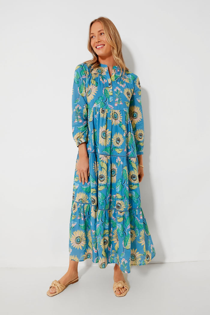 A woman wears a Ro's Garden cotton midi dress with a sunflower floral print and beige sandals, perfect for luxury travel wear.