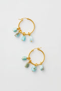 Lizzie Fortunato’s gold hoop earrings, each adorned with three dangling turquoise stone charms, beautifully highlight the art of handcrafted jewelry.