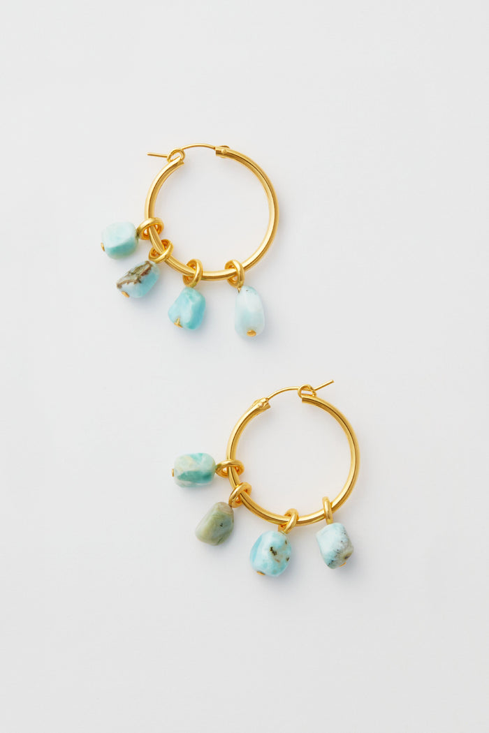 Lizzie Fortunato’s gold hoop earrings, each adorned with three dangling turquoise stone charms, beautifully highlight the art of handcrafted jewelry.
