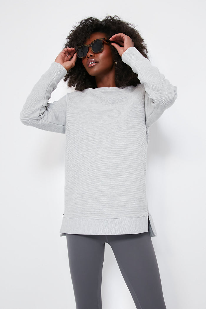A person in a light gray Varley oversized sweatshirt crafted from ottoman rib fabric and dark gray leggings adjusts their black sunglasses.