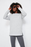 A person in a light gray Varley oversized sweatshirt crafted from ottoman rib fabric and dark gray leggings adjusts their black sunglasses.