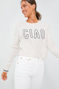 A woman wears the Z SUPPLY Milan Sweater in Light Oatmeal with "CIAO" on the front, styled with high-waisted white jeans. The relaxed fit of this cozy knit adds effortless style.
