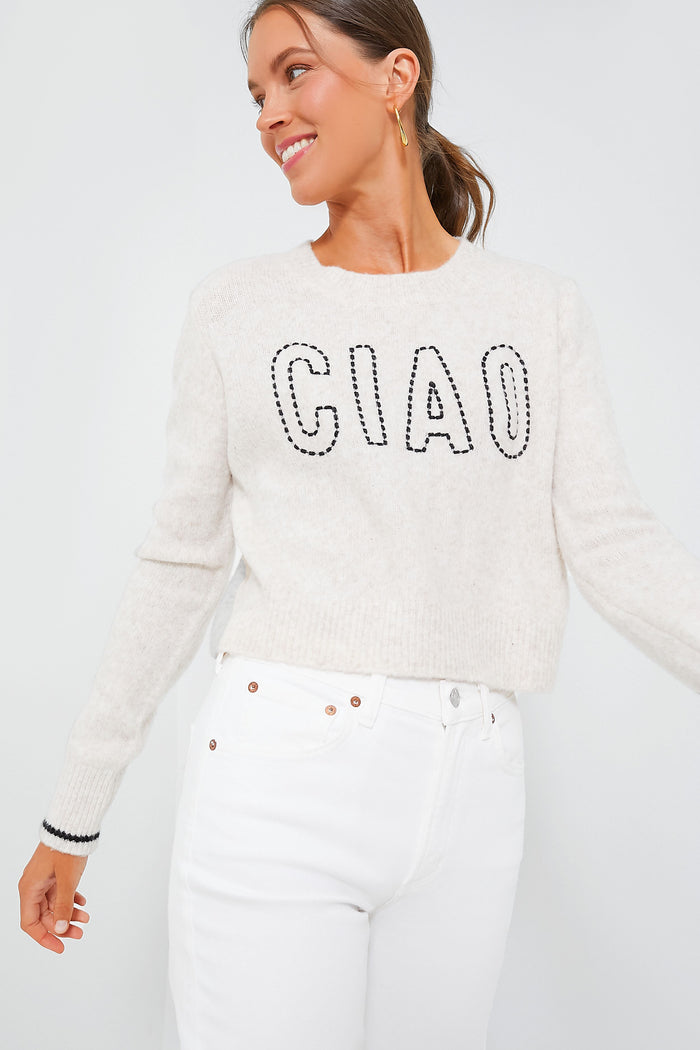 A woman wears the Z SUPPLY Milan Sweater in Light Oatmeal with "CIAO" on the front, styled with high-waisted white jeans. The relaxed fit of this cozy knit adds effortless style.