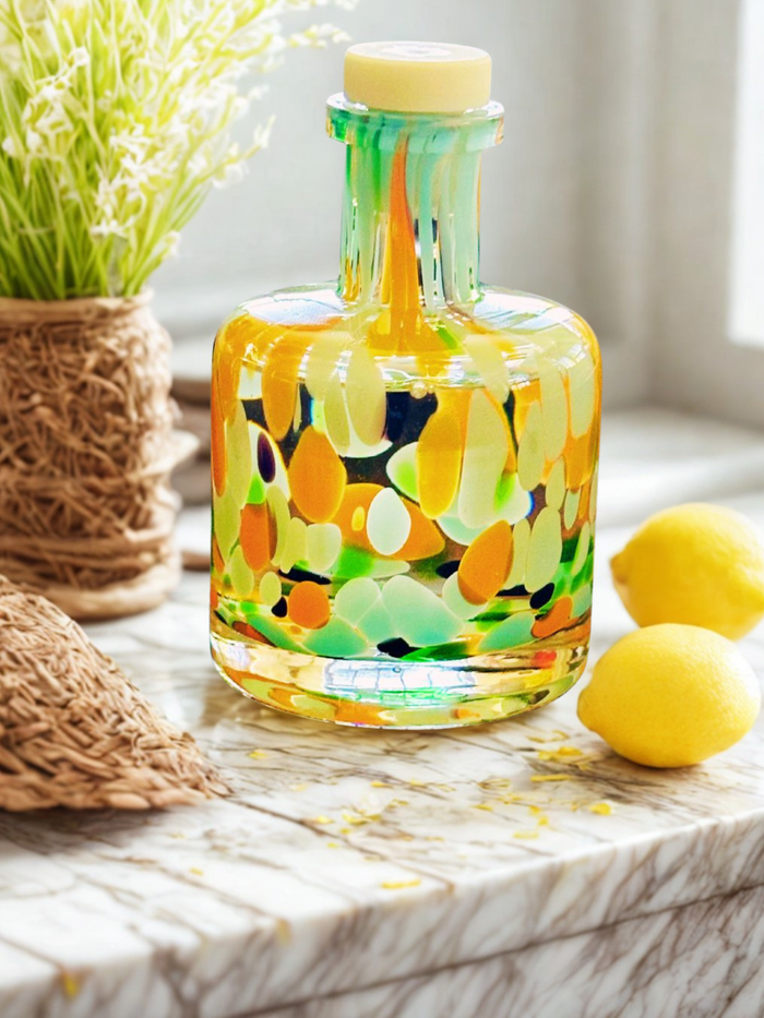 Shaped bottle of liquid with vibrant citrus colours on a marble counter with lemons.