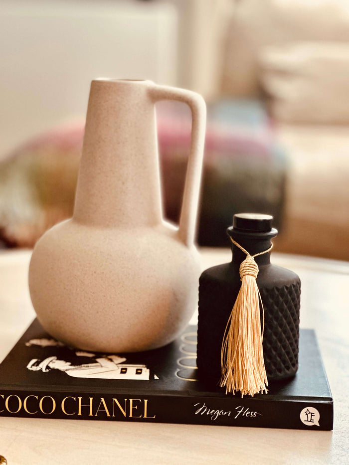 A luxury scented reed diffuser with a black glass vessel and a silk tassel, placed on a book.