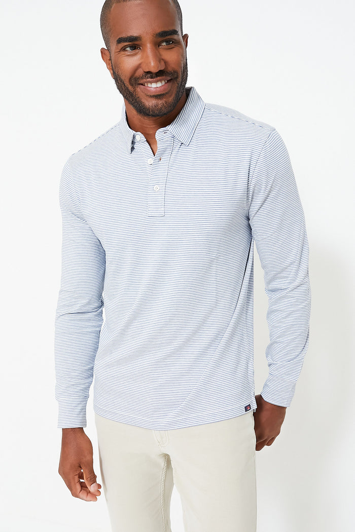 A man wears a Faherty light blue and white striped long sleeve polo shirt made from stretchy cotton blend, paired with light beige pants.