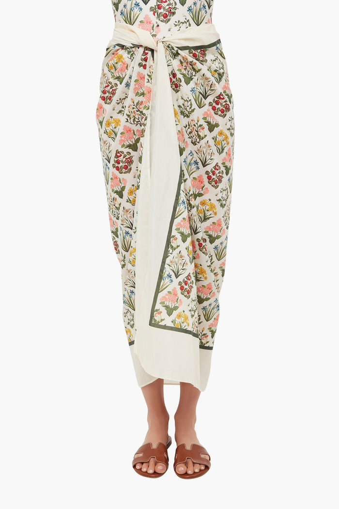 A person wears an AGUA BY AGUA BENDITA white floral-patterned handmade pareo wrap skirt with brown flat sandals, showcasing tropical prints ideal as a beach cover-up.