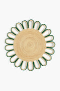 The Coro Cora round woven iraca palm placemat features a natural center, green-trimmed petal loops, and is handmade by Colombian artisans.