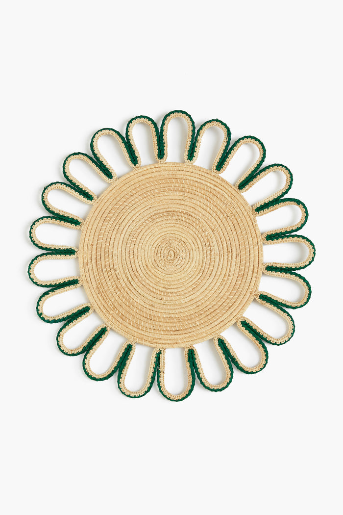 The Coro Cora round woven iraca palm placemat features a natural center, green-trimmed petal loops, and is handmade by Colombian artisans.