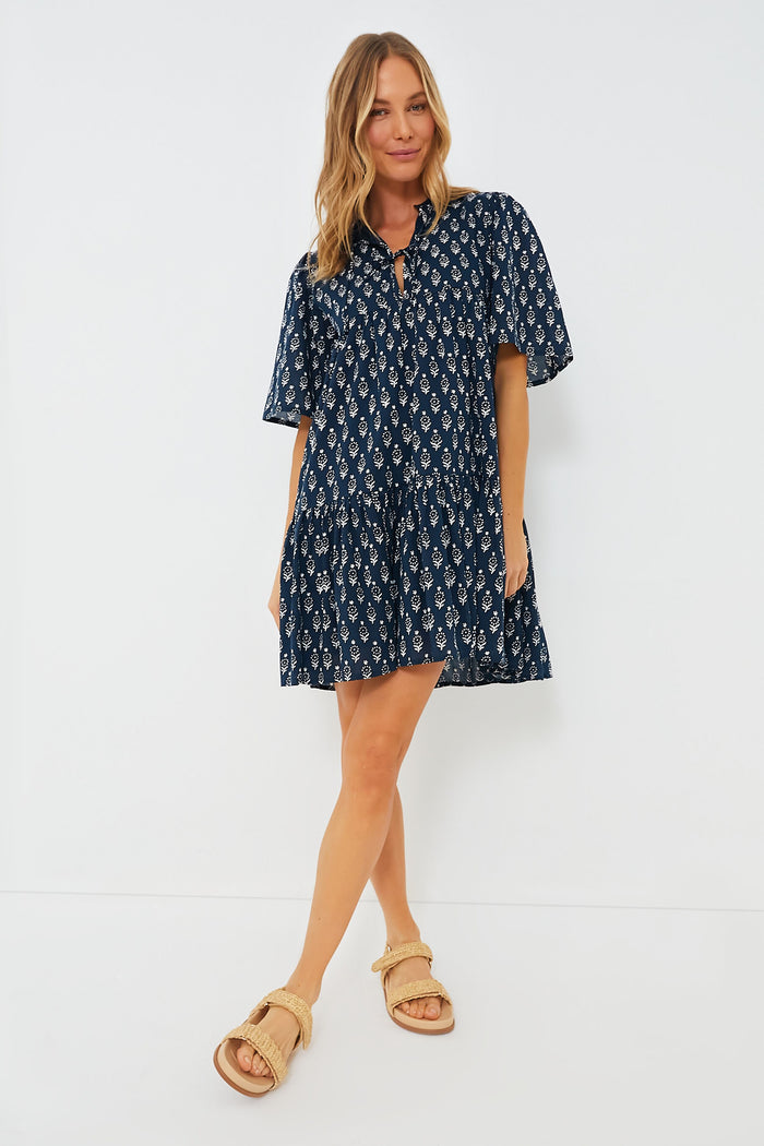 A woman wears a navy blue hand block printed short-sleeve organic cotton dress from Love, Tomas, paired with beige sandals.